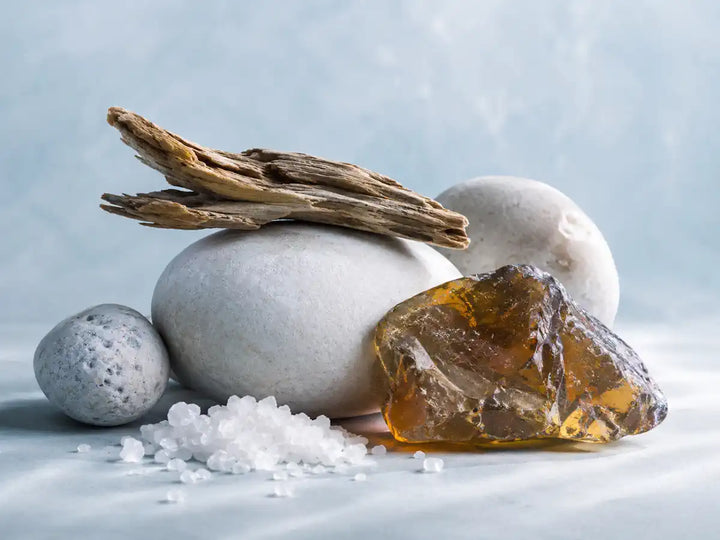 Mineral stones, sea salt, driftwood and amber-grey material representing a vegan ambergris accord