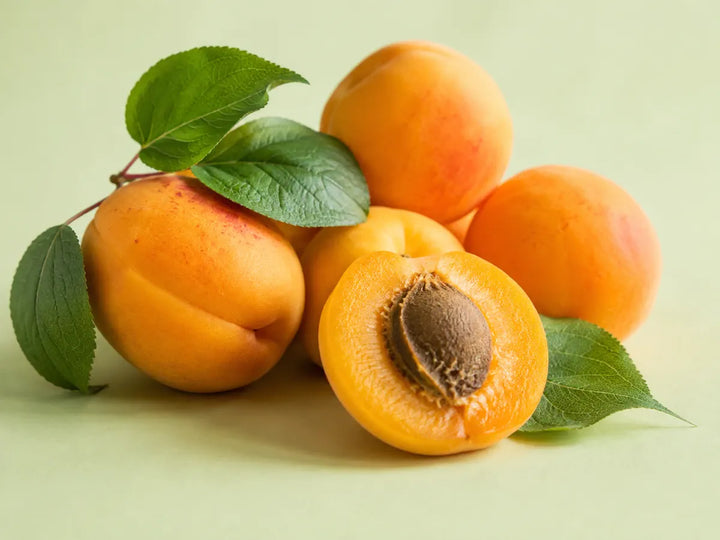 Ripe golden apricots, one sliced fruit and green leaves on a pale pistachio background