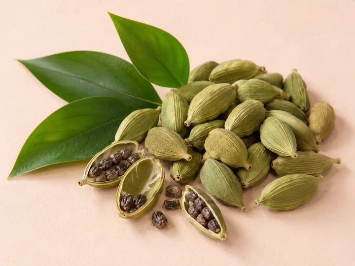 Green cardamom pods, opened pods and dark seeds on a light pale peach background