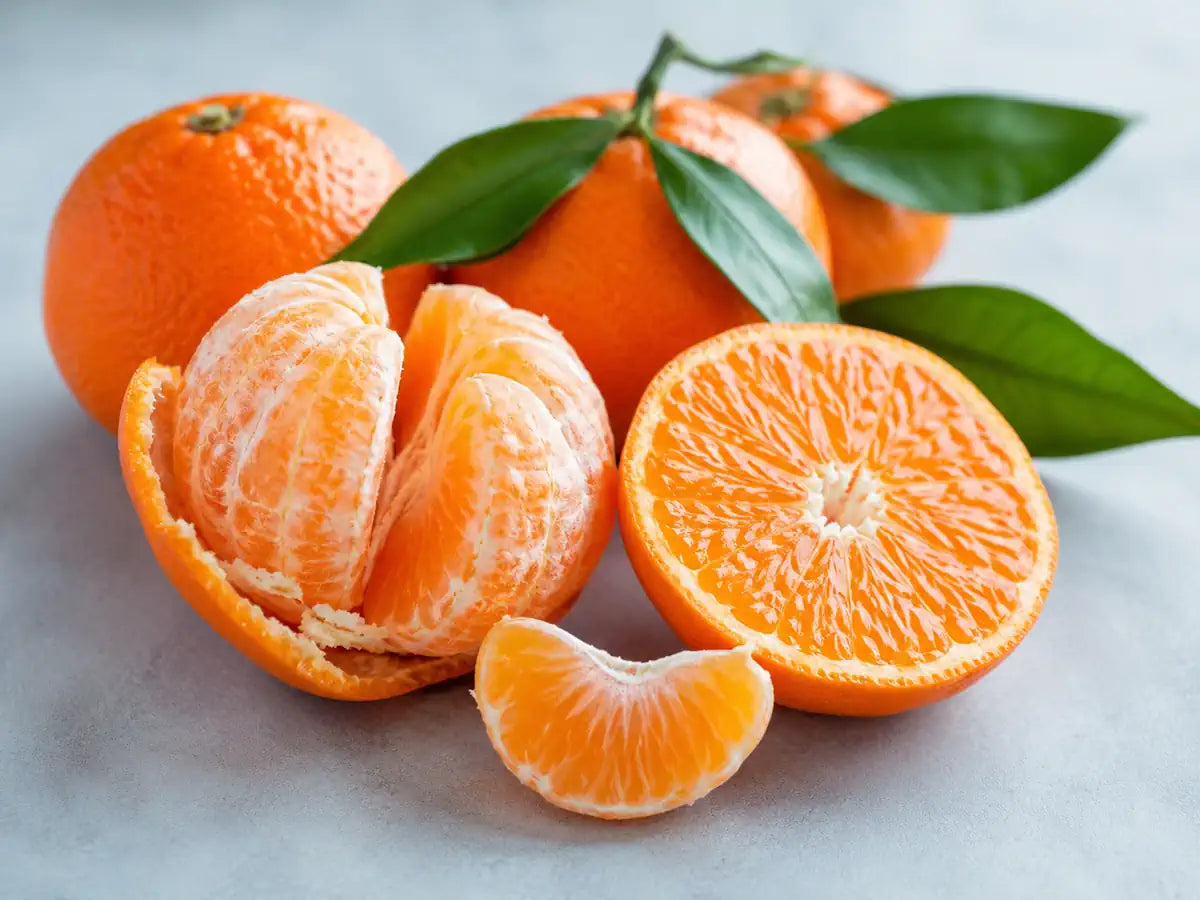 Fresh clementines, one peeled and one sliced, with green leaves on a pale blue-grey background