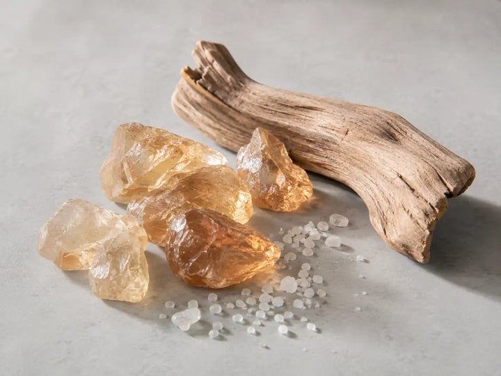 Pale amber-toned crystals, smooth driftwood and sea salt representing the mineral character of Ambroxan