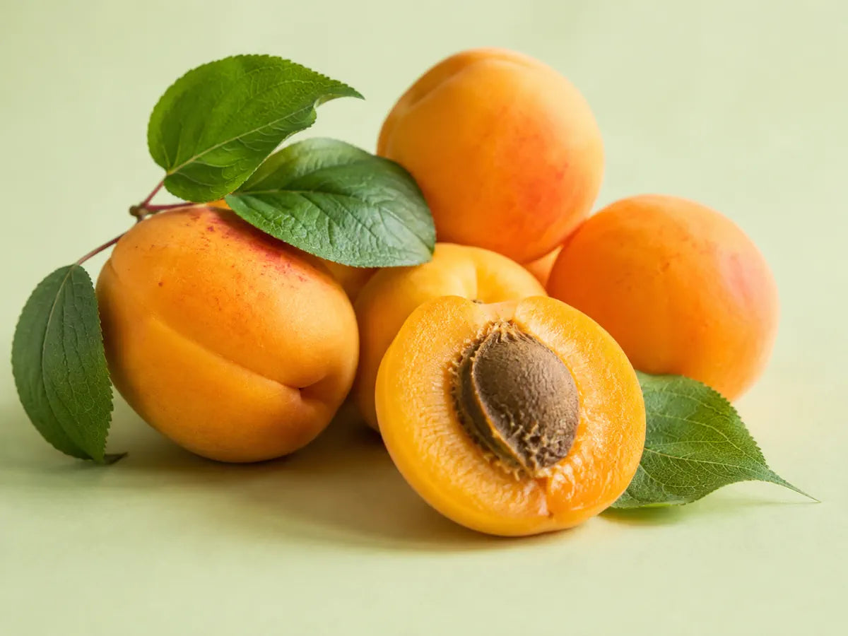Ripe golden apricots, one sliced fruit and green leaves on a pale pistachio background
