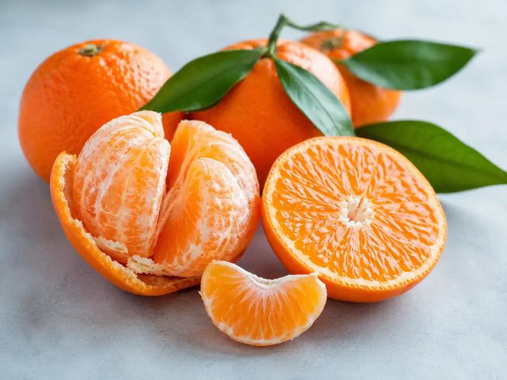 Fresh clementines, one peeled and one sliced, with green leaves on a pale blue-grey background
