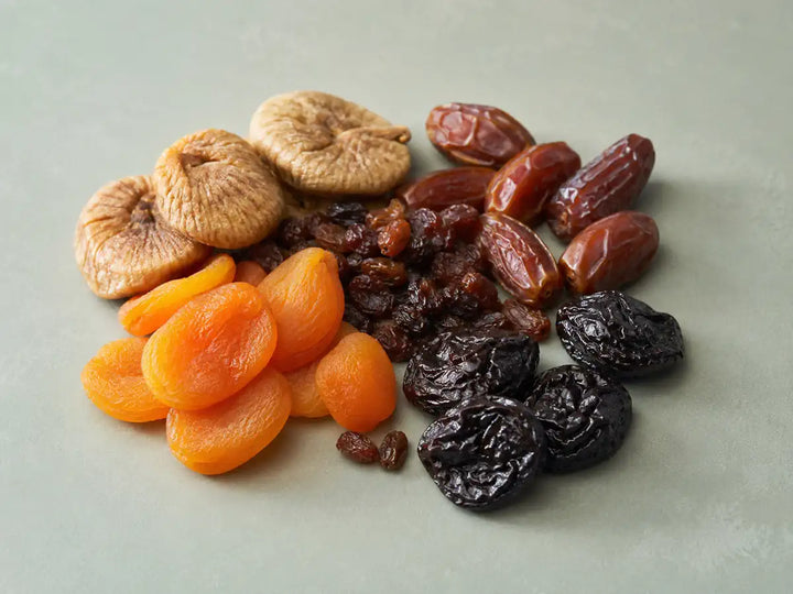 Dried figs, apricots, dates, raisins and prunes on a pale sage-grey background