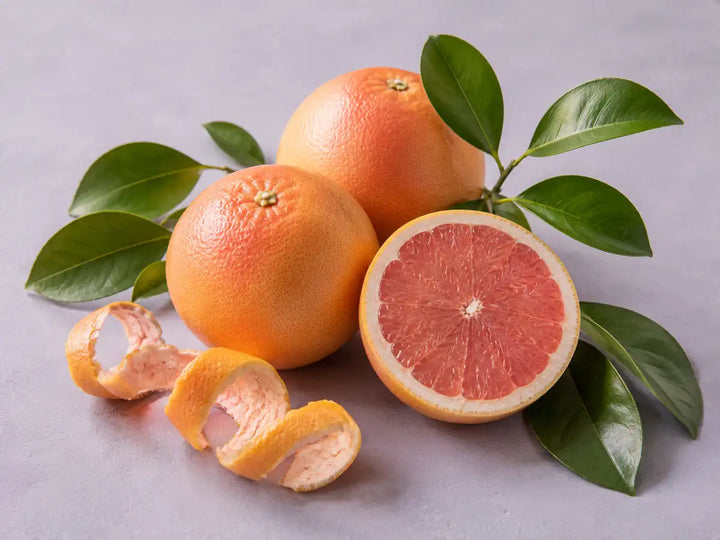 Pink grapefruit halves, curled peel and green leaves on a light lavender-grey background