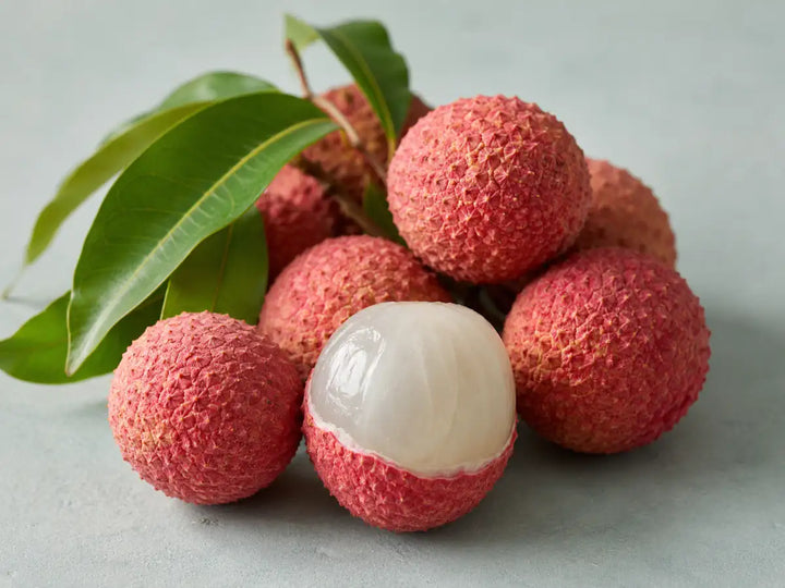 Ripe pink lychees, one peeled open, with green leaves on a pale mint-grey background