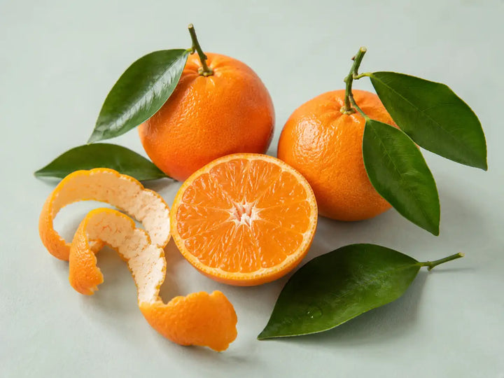 Fresh mandarins, curled peel and glossy green leaves on a light pale mint background