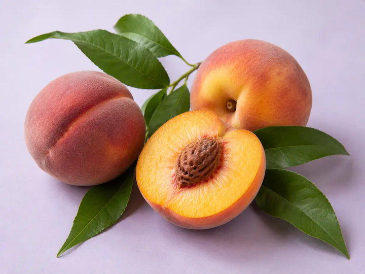 Ripe peaches, one sliced in half, with green leaves on a light pale lavender background