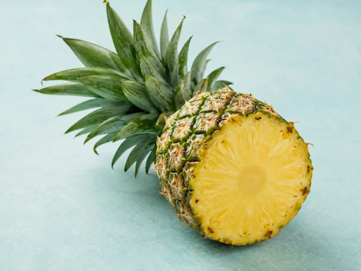 Fresh pineapple partly sliced with green leaves on a soft aqua background