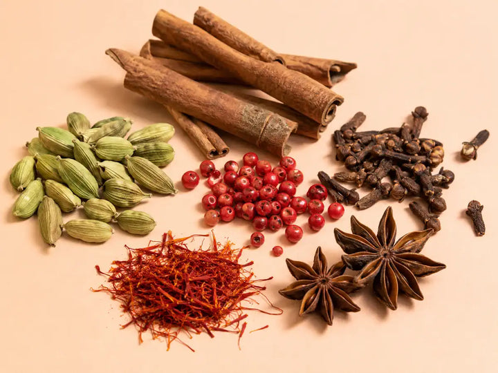 Cardamom, cinnamon, cloves, pink peppercorns, saffron and star anise on a pale apricot background