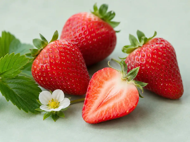 Ripe strawberries, one sliced fruit and a white flower on a light mint-grey background